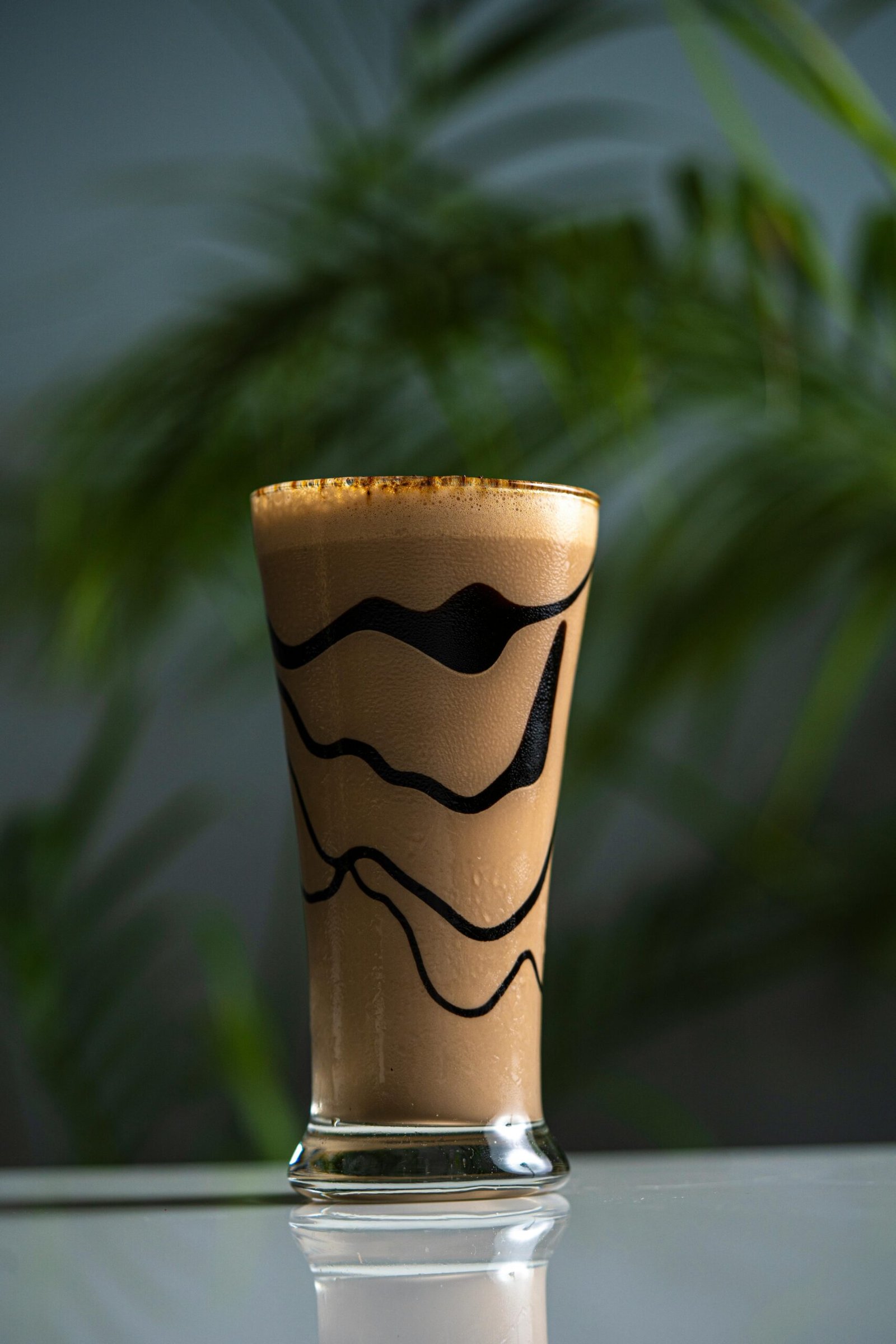 Tall glass of creamy chocolate shake with artistic swirls, perfect for refreshing indulgence.